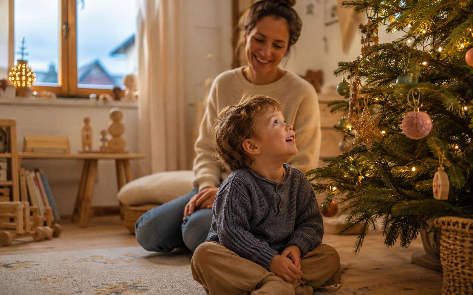 Glückliches Kind mit seiner Mutter vor dem Weihnachtsbaum